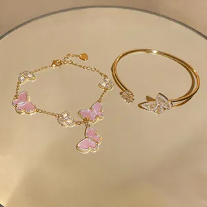 Close-up of a pink butterfly charm bracelet and a golden zircon butterfly open bangle.