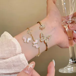 Close-up detail of gold butterfly bangle and pink shell butterfly bracelet on model's wrist