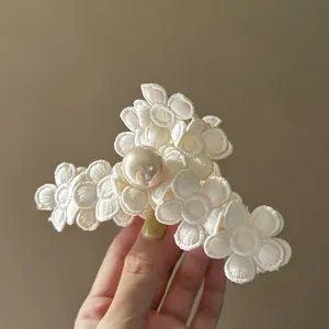 Détail d'une pince à cheveux vintage française avec fleurs brodées blanches et perle centrale