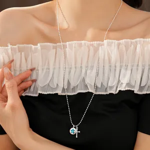 Detail showing a silver beaded necklace with a blue star pendant and a cross on a model