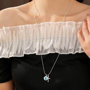Detail shot of a silver ball chain necklace with blue star and cross pendants on a model.