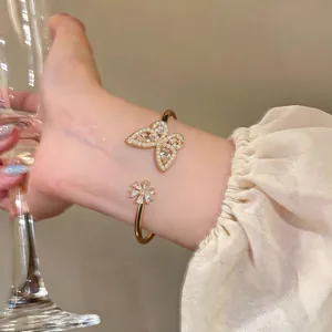 Close-up detail of a gold bangle featuring a pearl butterfly and zircon flower ornament.