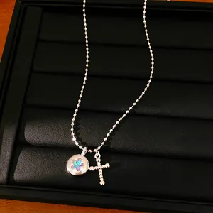Close-up of silver-tone necklace with iridescent star and beaded cross pendants on black tray.