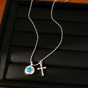 Macro detail of a silver ball chain necklace with a blue star inlay and beaded cross charm.