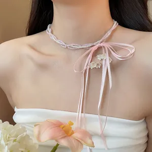 Close-up of sweet pink bow ribbon beaded pearl necklace on a female model's neck.