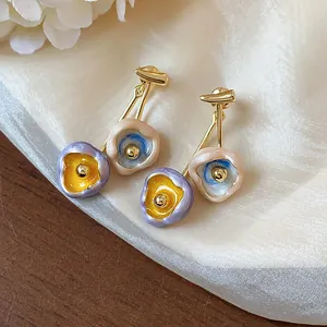 Detail shot of artistic drip oil earrings with colorful flower patterns and gold finish.