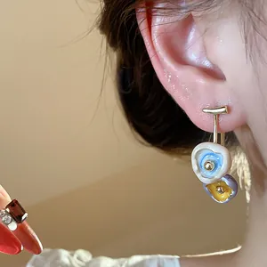 Detailed close-up of 18k gold-plated enamel drip oil stud earrings worn on a model's ear.
