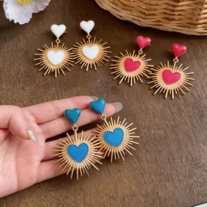 Dettaglio di orecchini a cuore in smalto colorato con design a raggiera dorata su legno