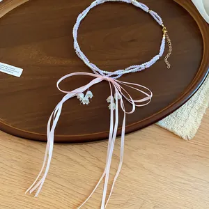 Detail view of sweet pink bow beaded necklace with white lily-of-the-valley charms on tray