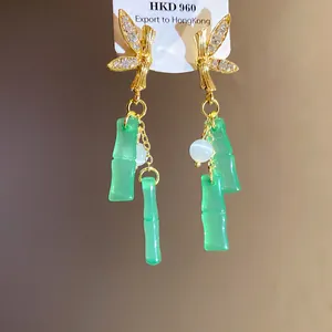 Primo piano di orecchini pendenti a nappa in bambù resina verde con strass e finitura oro.