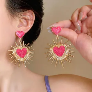 Dettaglio di orecchini vintage a cuore in oro con smalto rosa e motivo a raggiera dorata.