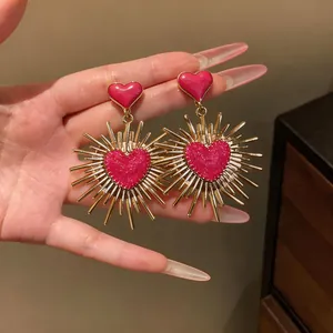 Dettaglio di orecchini a cuore vintage con raggi solari e centri rosa scintillanti.