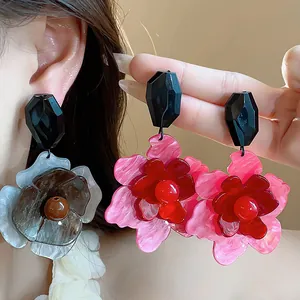 Primer plano de pendientes de flores de acrílico exagerados en tonos rosa y gris