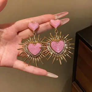 Primo piano di eleganti orecchini a cuore in smalto rosa con raggi solari dorati retrò