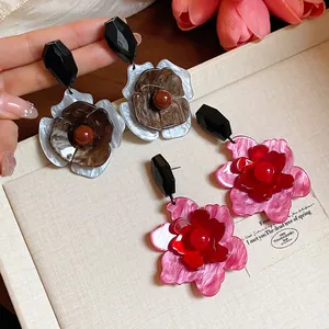 Primer plano de aretes de flores acrílicas grandes en rosa vintage y tonos marrones.