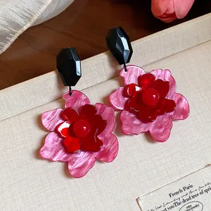 Primer plano de pendientes de flores de acrílico rosa y rojo sobre fondo beige