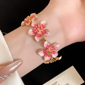 Vista dettagliata di un bracciale a fiori in smalto rosa con accenti metallici dorati.