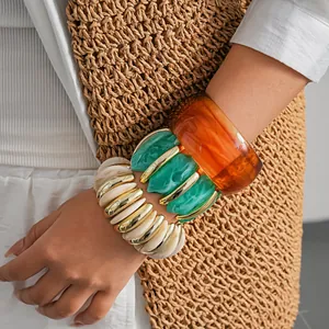 Primo piano di bracciali a strati in resina acrilica con trame in marmo e ambra sul polso femminile.