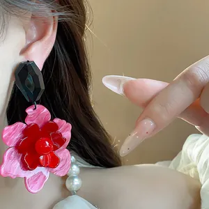 Primer plano de un pendiente de flor de acrílico con pétalos rosas y rojos en la oreja