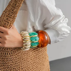 Primo piano dettagliato che mostra grossi bracciali in acrilico marmorizzato ambra e verde.