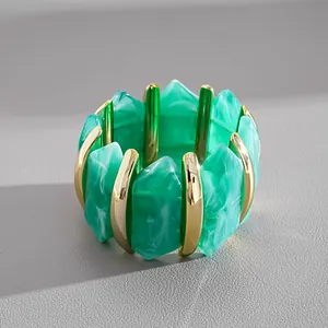 Primo piano di un bracciale rigido geometrico in acrilico marmorizzato verde e oro.