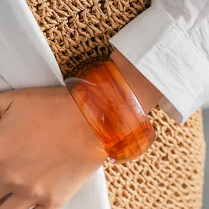 Primo piano di un bracciale rigido vintage in acrilico ambra marmorizzato indossato al polso con borsa