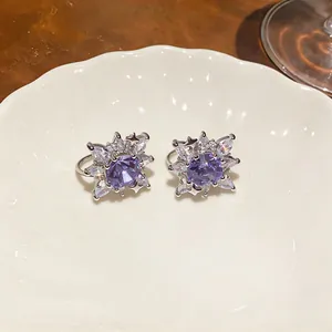 Detailed close-up of sparkly purple zircon flower ear clips on a white ceramic plate.