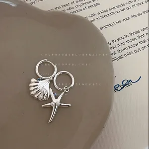 Primo piano di orecchini asimmetrici in argento con stella marina e conchiglia