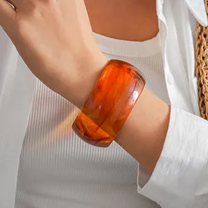 Primo piano di un elegante bracciale rigido in acrilico marmorizzato arancione al polso