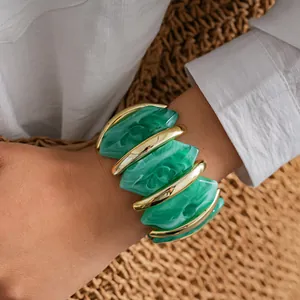 Dettaglio di un bracciale a polsino in acrilico marmorizzato verde con barre oro