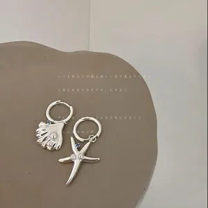 Dettaglio di orecchini asimmetrici in argento con ciondoli a conchiglia e stella marina e perle