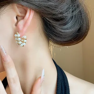 Close-up of elegant French retro C-shaped earrings with white pearls and zircons on ear.