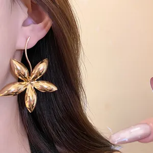 Detaillierte Makroansicht eines großen goldpolierten Blumenstern-Ohrrings am Modellohr