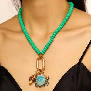 Detalle de un collar de cuentas turquesas con dijes de concha y cangrejo en una modelo real.
