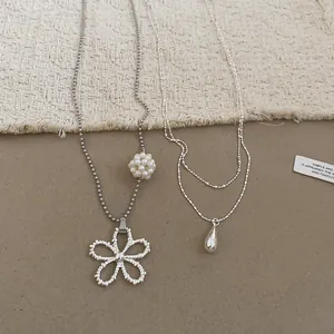 Close-up of double-layer teardrop and hollow flower pearl necklaces on soft textured background.