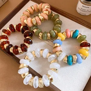 Detailed view of assorted dyed resin bracelets with gold spacers in a wooden tray.