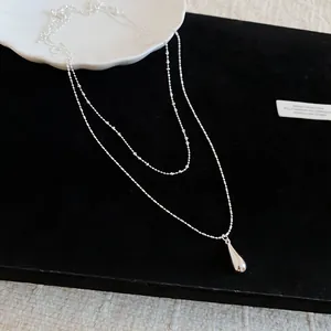 Close-up view of a double-layered silver necklace featuring a sleek teardrop pendant