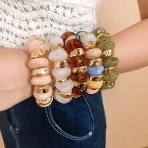 Close-up of stacked colorful resin beads and gold textured chunky bracelets on arm