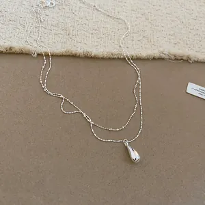 Detail view of a minimalist silver double-layer necklace with a sleek waterdrop pendant