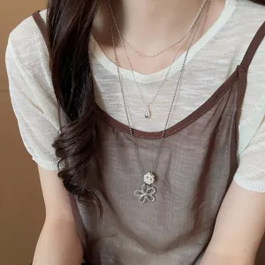 Close-up of layered silver necklace with pearl flower and water drop charms on model