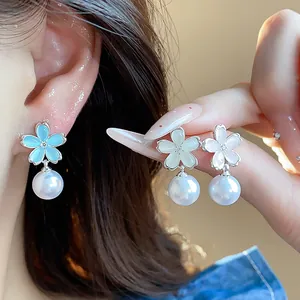 Detail view of flower and pearl drop earrings shown on an ear and held by a manicured hand.