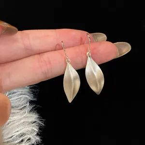 Dettaglio ravvicinato di orecchini pendenti a forma di foglia in argento spazzolato opaco.