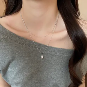 Macro view of layered silver-toned necklace with sleek teardrop pendant on model