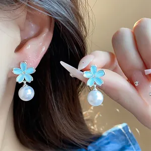 Close-up detail of blue flower earrings with dangling pearls and zircon accents