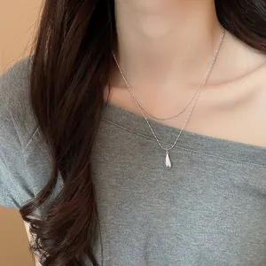 Close-up view of a minimalist silver double-layer necklace featuring a sleek teardrop pendant