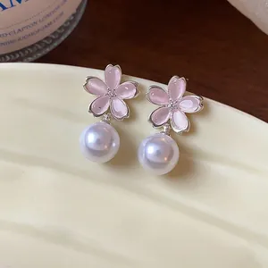 Detail view of pink cherry blossom earrings with white pearls on a ceramic plate.