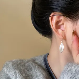 Vista dettagliata di orecchini pendenti a foglia geometrica in argento su una modella.