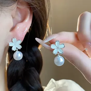 Close-up of elegant flower stud earrings with white pearl drop on model's ear