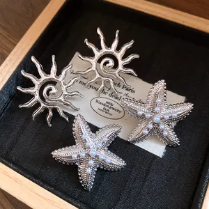 Dettaglio di orecchini a lobo a forma di stella marina e sole con perle argentate