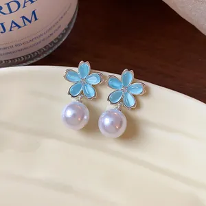 Close-up of elegant flower earrings with light blue petals and dangling white pearls